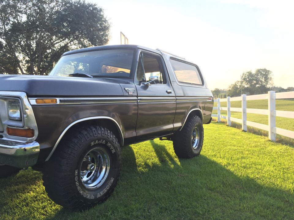 1978 Ford Bronco parked on grass next to a white fence