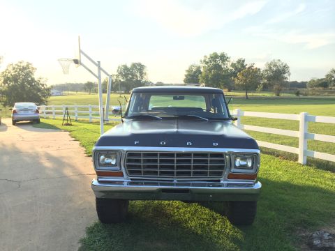 1978 Ford Bronco - A dark blue Ford truck is parked outside on a sunny day with a white fence and green fields in the background.