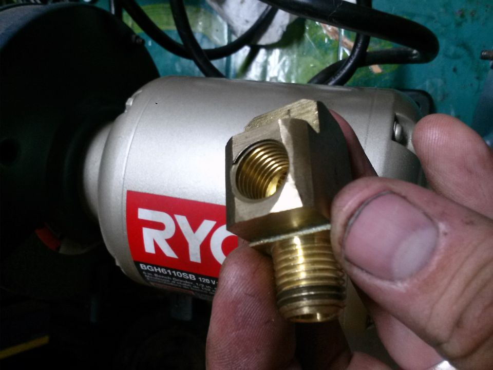 Brass fitting with threaded ends held in front of a Ryobi grinder
