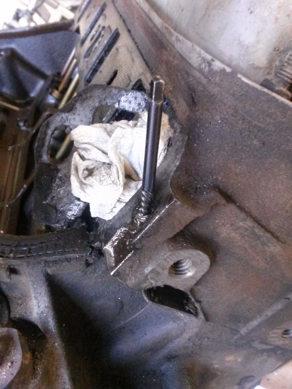 Close-up of a metal engine component with a bolt sticking out and a rag stuffed in a hole