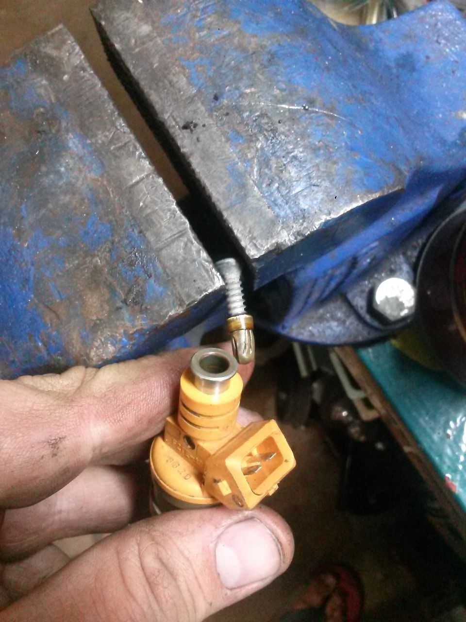 Orange fuel injector held by hand, clamped in a blue vise