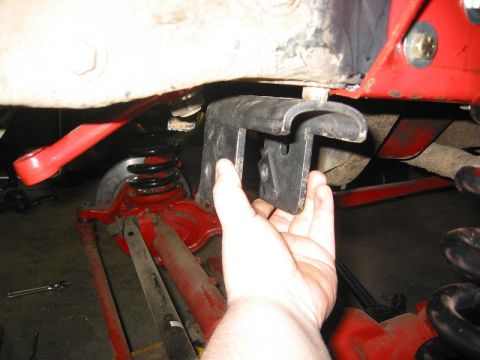 1985 Ford Bronco - A metal bracket is being held near the suspension of a vehicle, possibly for modification.