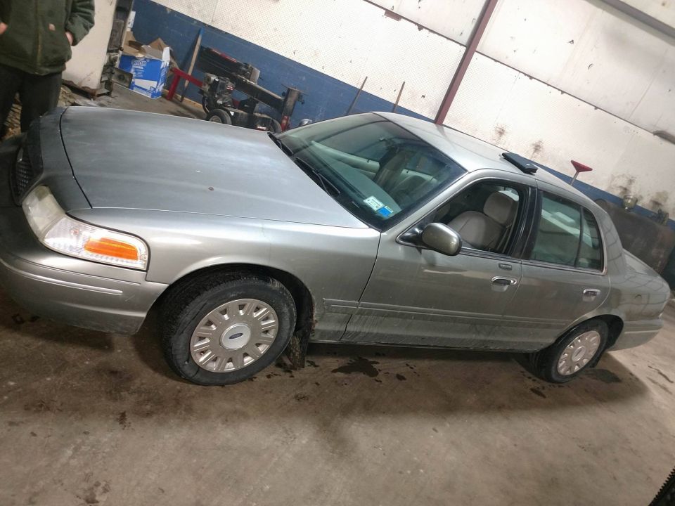 Silver-gold Ford Crown Victoria sedan parked inside a shop