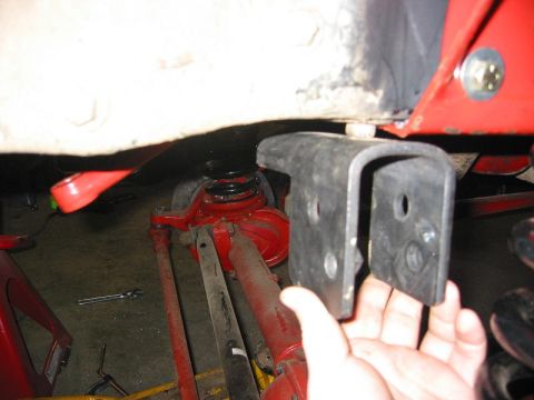 1985 Ford Bronco - A hand holds a metal bracket near the red suspension system of a vehicle, suggesting a modification or repair.