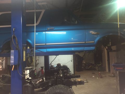 1995 Ford Bronco - A blue 1995 Ford Bronco is shown on a lift in a garage, with its engine removed for work.