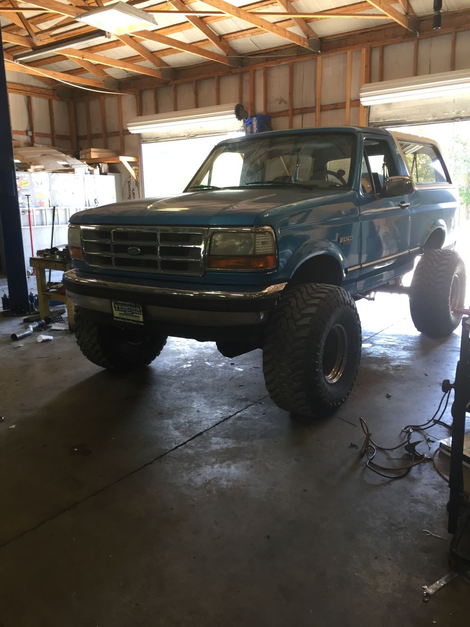 Lifted teal 1995 Ford Bronco with large off-road tires in a garage.