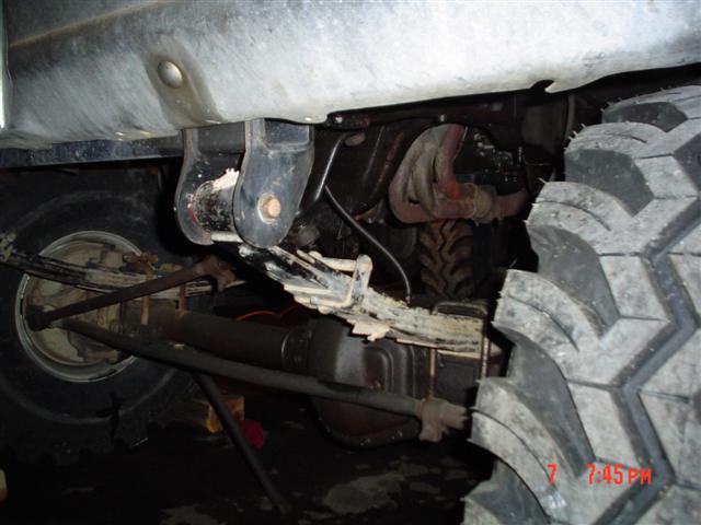 Underside of a lifted truck showing leaf springs, driveshaft and mud tire