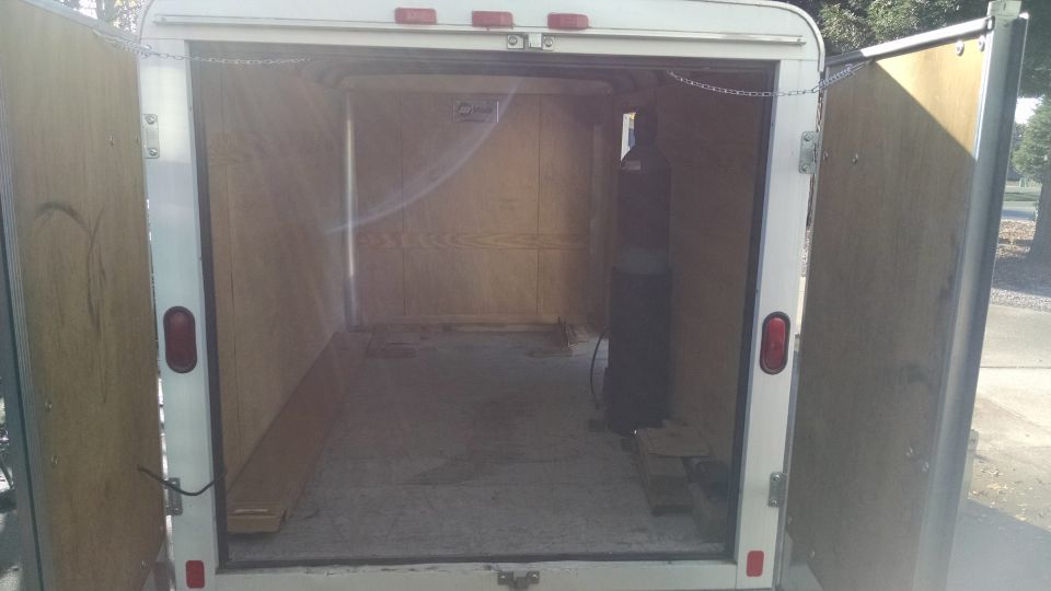 Interior of an empty cargo trailer with rear doors open. Tall cylinder on the right.