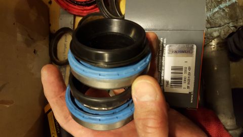 1994 Ford Bronco - A hand holds several stacked black and blue bearing seals. A box with a barcode and text is visible behind the seals.