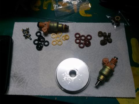 1996 Ford Bronco - Several fuel injectors and assorted o-rings and small parts are laid out on a white paper towel. A silver circular object is also visible.