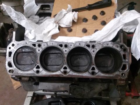 1996 Ford Bronco - A close-up view of the cylinder head deck of a V8 engine block, showing four cylinder bores. Several bolts and a screwdriver are visible on…