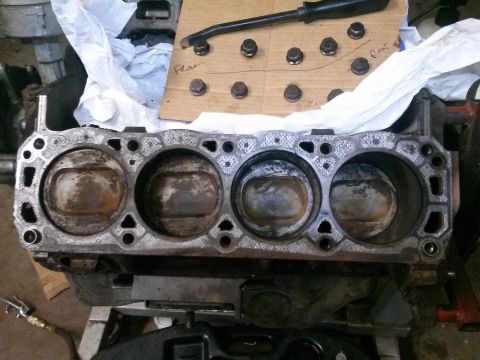 1996 Ford Bronco - A close-up view of the cylinder head of an engine block, showing four pistons within their cylinders. A cardboard piece with several bolts…