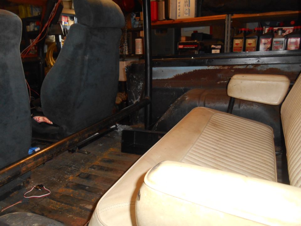 Interior of a vehicle with dark gray bucket seats and a tan bench seat, wooden floor.