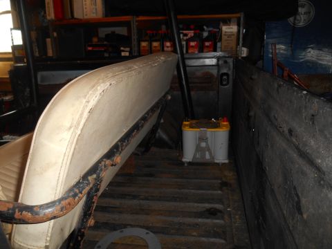 1972 Ford Bronco - The interior of a vehicle shows a white bench seat with a rusty metal frame and a yellow Optima battery in the cargo area.
