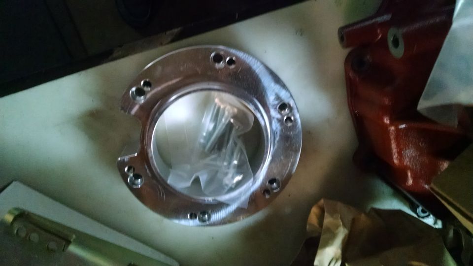 Shiny metal circular part with bolt holes and screws inside a plastic bag.