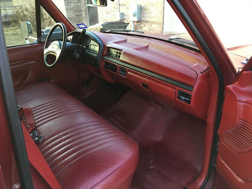 Red vinyl bench seat and red dash with CUSTOM badge inside a Ford F-150 cab, seen from passenger door