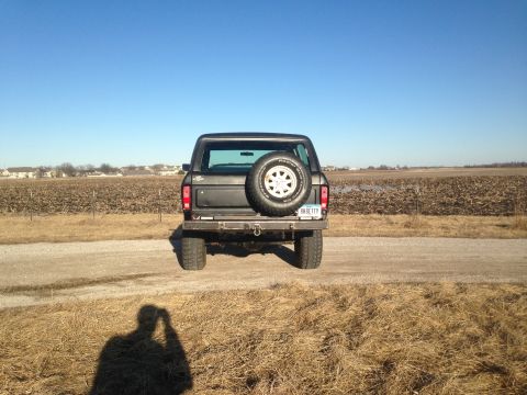 1979 Ford Bronco - The rear view of a black Ford Bronco parked on a dirt road with a spare tire mounted on the back. A license plate reading "BKBETTY" is visi…
