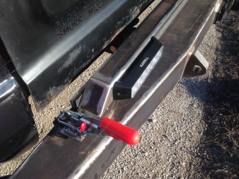 1979 Ford Bronco - A close-up view shows a black metal truck bed edge with embossed text and a heavy-duty metal bumper with a clamp and a black electronic dev…