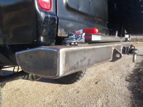 1979 Ford Bronco - The rear driver's side of a black pickup truck is shown, featuring a custom-fabricated steel bumper with a tow hitch receiver and a clevis…