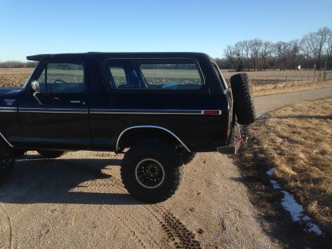 1979 Ford Bronco - The rear driver's side of a black 1979 Ford Bronco is shown parked on a dirt road with a spare tire mounted on the back. The vehicle is in…