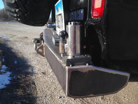 1979 Ford Bronco - The rear of a black SUV shows a custom metal bumper with a trailer hitch receiver and a spare tire mounted above. A license plate and a sma…