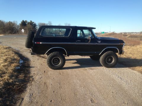 1979 Ford Bronco - A black 1979 Ford Bronco is parked on a gravel road with a spare tire mounted on the rear. The vehicle is viewed from the side with a clear…