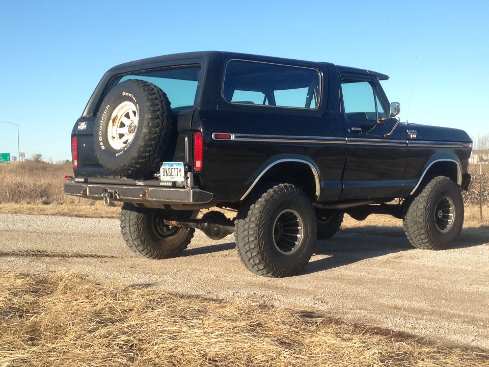 Black 1979 Ford Bronco rear driver's side view with spare tire and custom bumper.