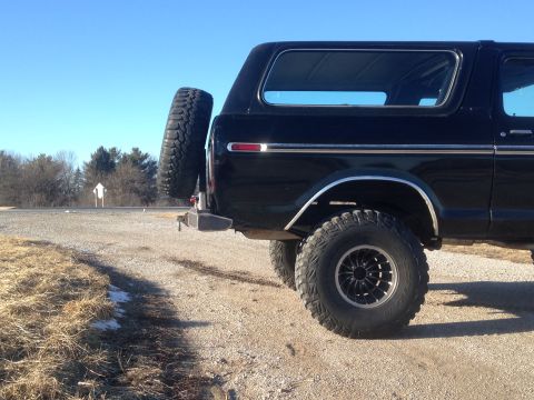 1979 Ford Bronco - The rear passenger side of a black Ford Bronco is shown parked on a gravel road with dry grass and a few patches of snow on the left. A spa…