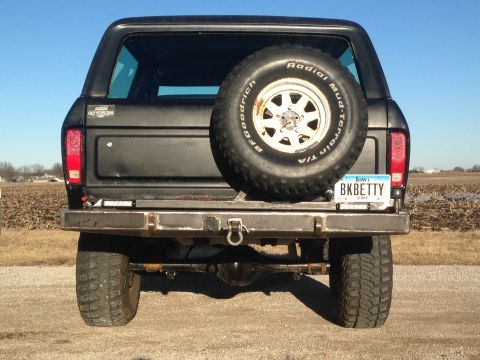 1979 Ford Bronco - The rear view of a black Ford Bronco with a spare tire mounted on the back. A custom metal bumper with a tow hitch and a license plate read…