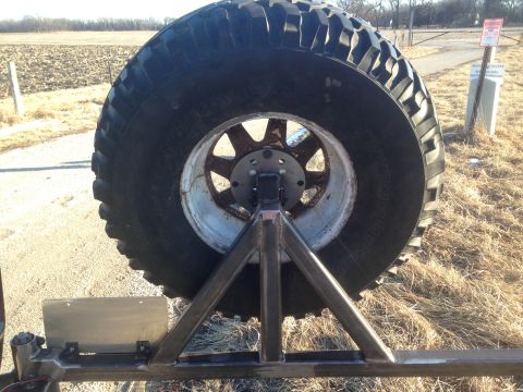 1979 Ford Bronco - A close-up rear view of a large off-road tire mounted on a custom steel frame, likely a spare tire carrier for a vehicle. The tire is mount…
