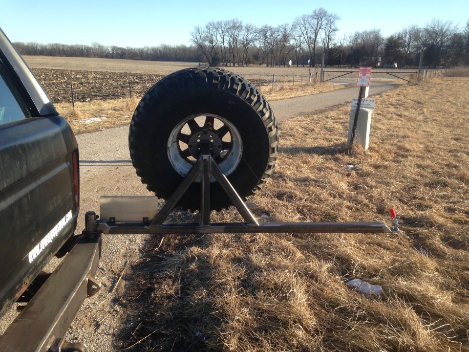 Rear view of a dark SUV with a large spare tire mounted on a custom rack.