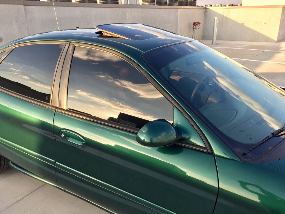 Dark green 1999 Ford Taurus sedan, driver's side, tinted windows, sunroof, sky reflection.