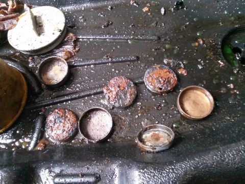 1996 Ford Bronco - A collection of small, rusty metal caps and a larger white cap with a metal insert are scattered across a dark, wet surface with debris.