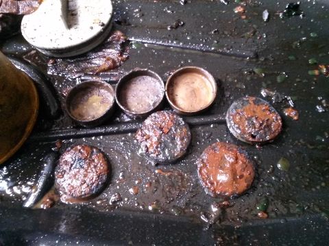 1996 Ford Bronco - Several small, round, metal caps or lids are scattered in a dark, wet surface, some covered in reddish-brown residue. A larger white object…