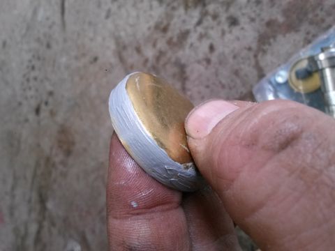 1996 Ford Bronco - A person's thumb and finger are holding a round, gold-colored object that has a white coating around its edge. The background is a textured…