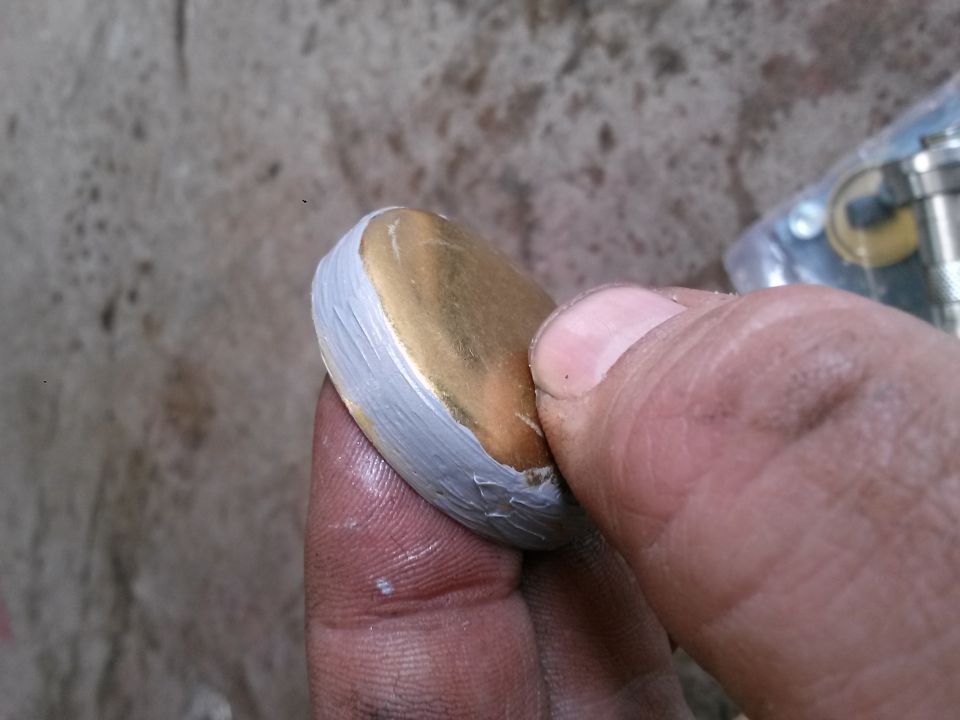 Close-up of a hand holding a round object with a gold surface and white edge.