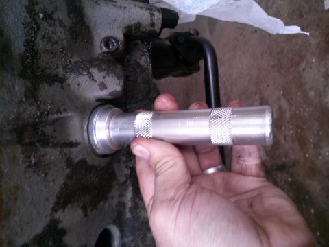 1996 Ford Bronco - A hand holds a silver knurled tool against a greasy, metallic housing, possibly part of a vehicle's drivetrain.