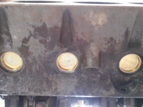 1996 Ford Bronco - A close-up view of the side of a cast iron engine block, featuring three brass freeze plugs. The freeze plugs have visible markings, with o…