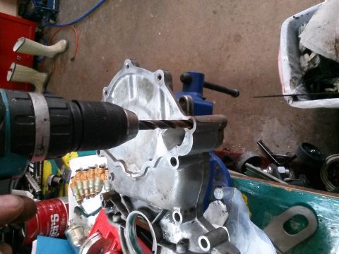 1996 Ford Bronco - A close-up view shows a drill with a bit drilling into a silver-colored automotive part held in a blue vise. Several fuel injectors are vis…