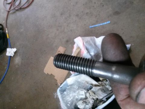 1996 Ford Bronco - A close-up shot of a threaded metal rod held by a hand. The background shows a concrete floor with various items including an air hose and…