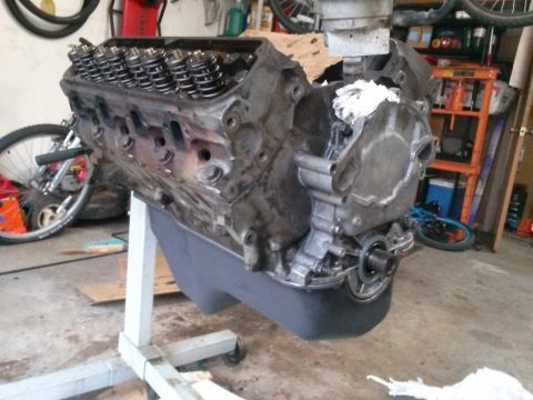 1996 Ford Bronco - A disassembled V8 engine is mounted on a white engine stand in a garage. The engine block, cylinder heads with valve springs, and part of t…