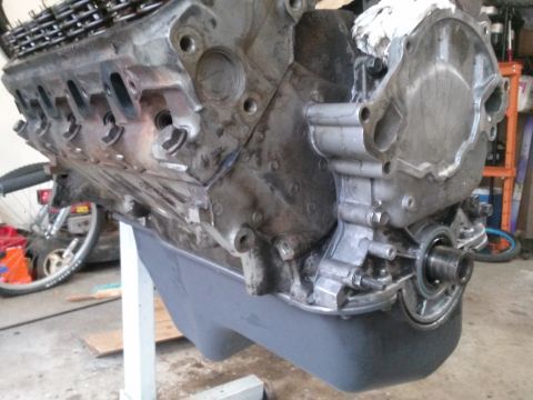 1996 Ford Bronco - A close-up view of a V8 engine block with the oil pan installed, mounted on a white stand. The engine appears to be undergoing maintenance…