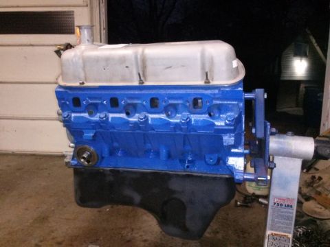 1996 Ford Bronco - A blue engine block with a silver valve cover is mounted on an engine stand. The engine is in a garage setting with a garage door in the ba…