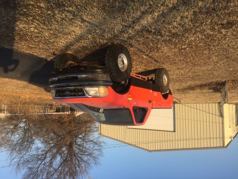 1982 Ford Bronco - A lifted, bright orange Ford pickup truck with large off-road tires is parked in front of a white garage door. The truck has a black trim a…
