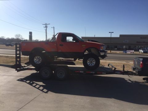 1982 Ford Bronco - A lifted orange and black Ford F-150 pickup truck is loaded onto a flatbed trailer. The truck is viewed from the side, with its front end e…