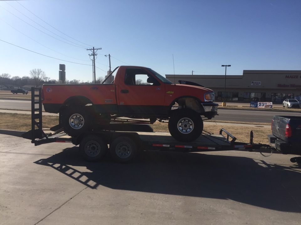 Lifted orange and black Ford F-150 pickup truck on a flatbed trailer.