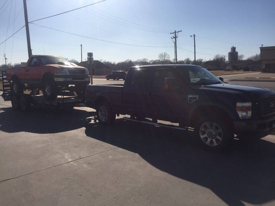 Dark blue Ford F-250 towing a trailer with an orange Ford pickup truck.