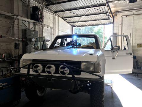 1990 Ford Bronco - Photo of a white Ford off-road pickup with auxiliary lights in a garage, not a technical document.