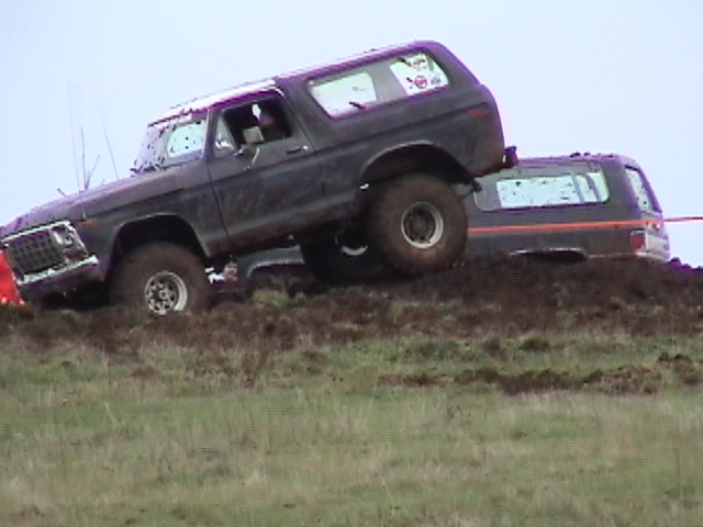 Muddy purple Ford Bronco climbing a mud pit with front wheel lifted