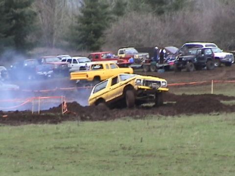 1994 Ford Explorer - Off-road SUV navigates a muddy track during an event, with several other vehicles parked nearby.